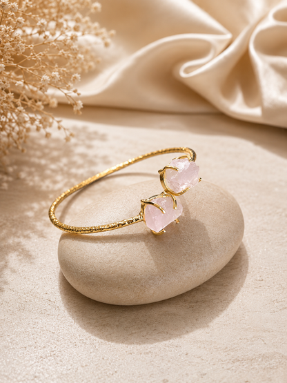 Gold bracelet with pink stones on a stone surface with beige fabric and dried flowers in the background